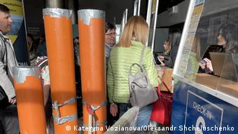 People at a check-in counter, three tall orange sewage pipes stand next to them.